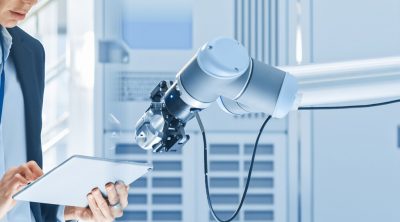Stylish Female Industrial Robotics Engineer Uses Tablet Computer to Program and Manipulate Robot Arm for Lifting, Moving Objects. Technology Research Facility for Machine Learning and Cloud Computing